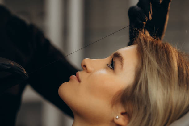 Stylist using thread for eyebrow shaping on woman in salon