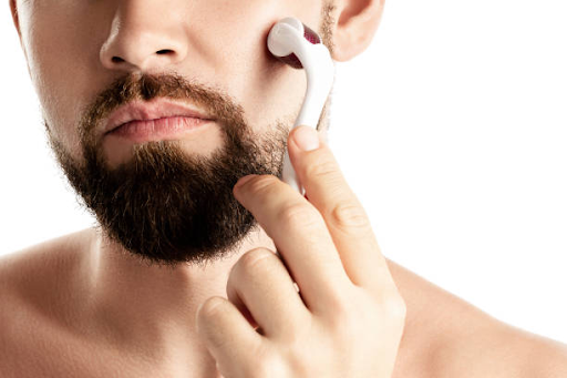 Man using facial roller on his beard and jawline against a white background.